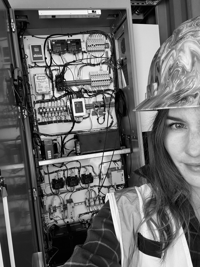 Devyn Pizzo inspecting electrical switchgear control cabinet in hard hat and safety vest